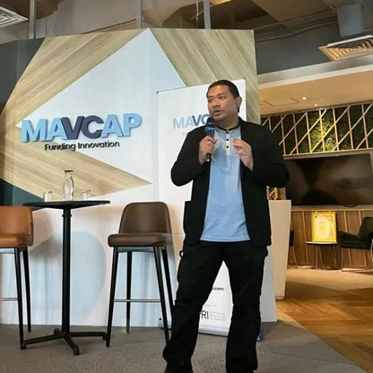 Hafiz Zainudin presenting at MAVCAP Funding Innovation event, speaking into microphone with Growth Charger banner in background